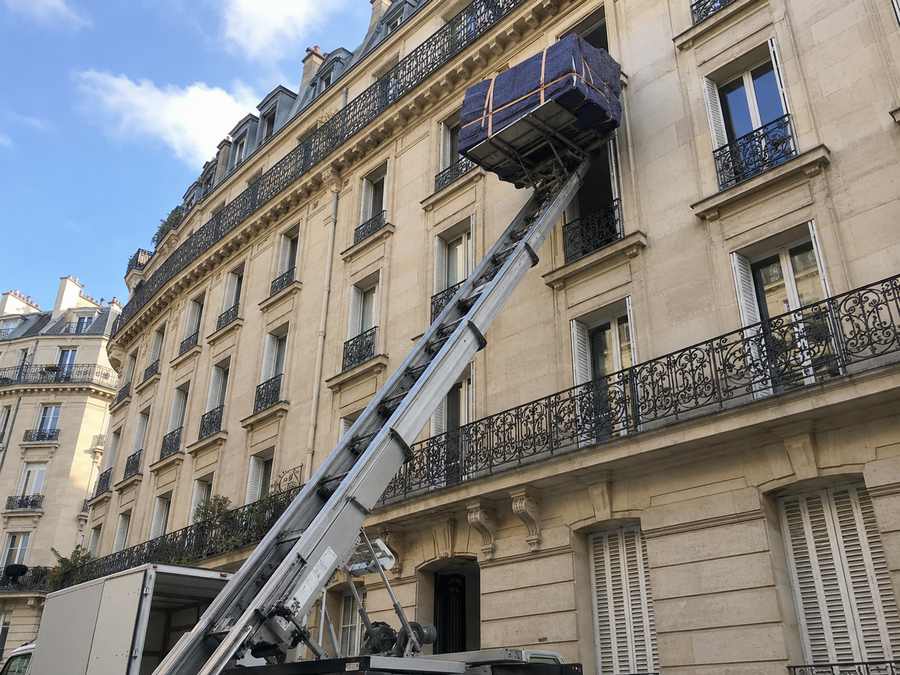 Monte-meubles déployé contre la façade d'un immeuble parisien, charge à hauteur d'étage