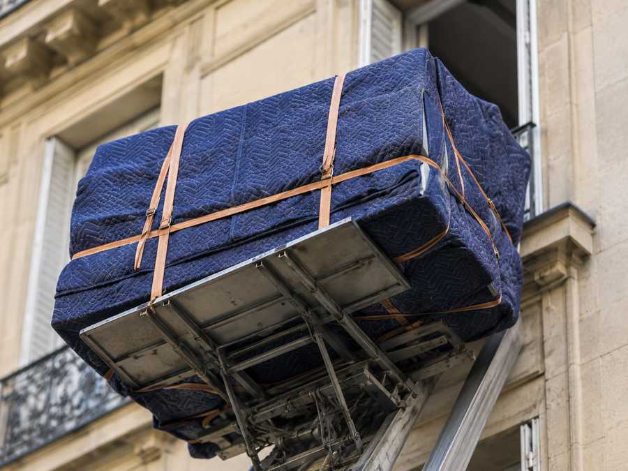 Plateforme de monte-meubles chargée d'un meuble sanglé devant une fenêtre ouverte